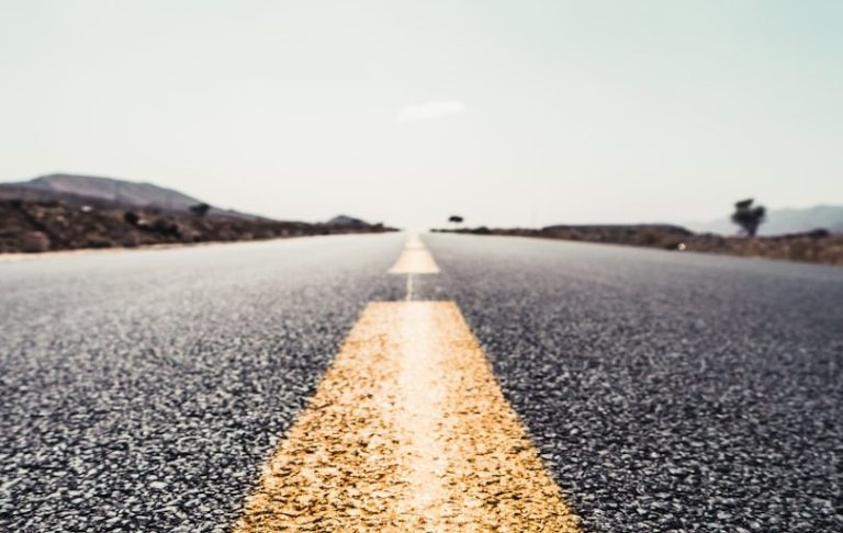 Leadership Coaching und Unternehmensberatung Eine leere Straße mit gelber Mittelmarkierung und bergiger Landschaft im Hintergrund.