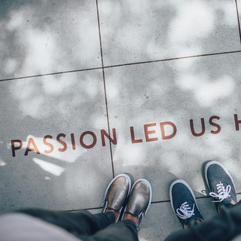 Leadership Coaching Sicht auf den Boden mit dem Schriftzug „Passion led us here“ und zwei Paar Schuhen.